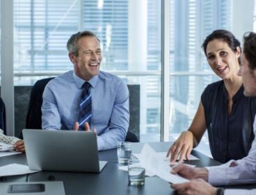 A diverse business team collaborating around a modern conference table with a laptop and papers.